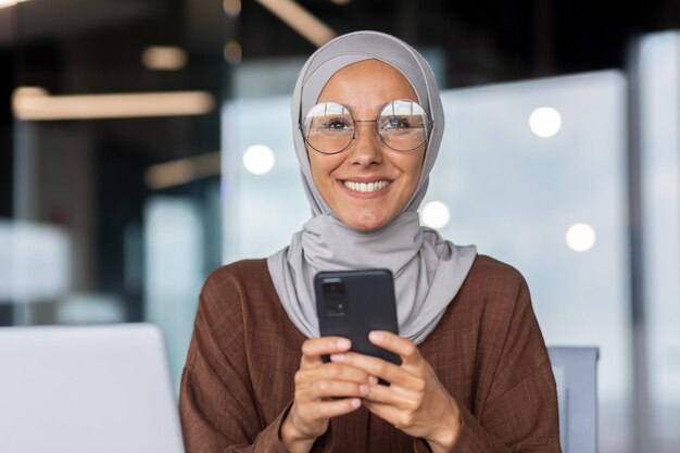 Retrato de uma jovem e bela estudante muçulmana em hijab que está segurando e usando o telefone olhando