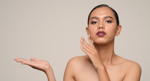 Retrato de uma jovem e bela modelo feminino, sorrindo e mostrando a palma da mão vazia para inserir e apresentar seu produto na parede cinza