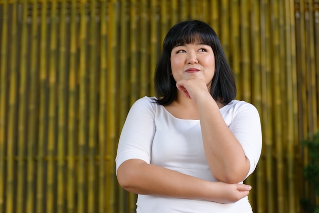 Retrato de uma jovem e bela mulher asiática com excesso de peso contra uma parede de bambu ao ar livre