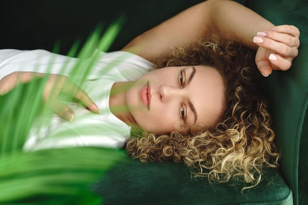 Retrato de uma jovem e bela mulher com cabelos cacheados, deitada no sofá verde