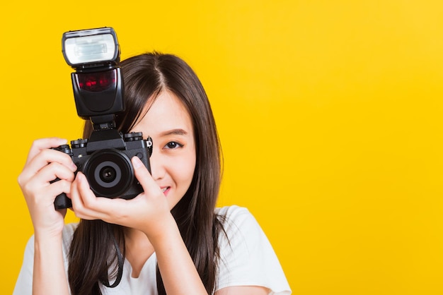 Retrato de uma jovem e bonita fotógrafa asiática sorridente tira uma foto e olha o visor em uma câmera fotográfica sem espelho digital retrô pronta para fotografar, tiro em estúdio isolado em fundo amarelo