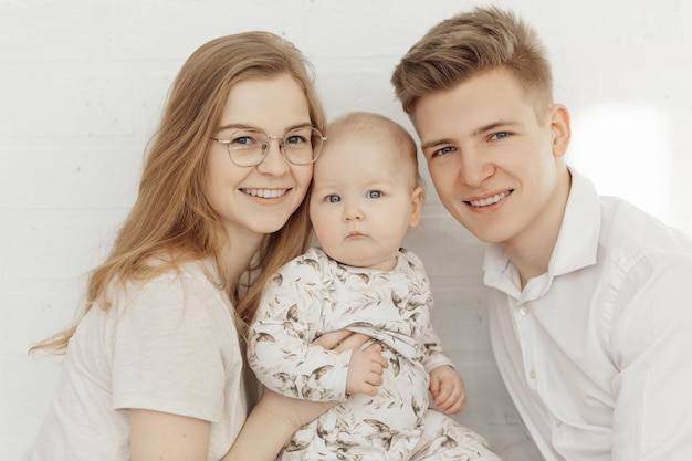 Retrato de uma jovem e feliz família sorridente com um bebê infantil de olhos azuis querubins em roupas brancas sentadas
