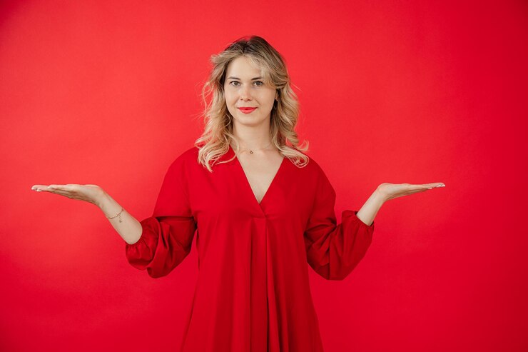 Foto retrato de uma jovem elegante em um vestido vermelho brilhante espalhando os braços para os lados isolados em fundo vermelho mostrando anúncio de resultado lindo visual moderno indústria da moda e beleza