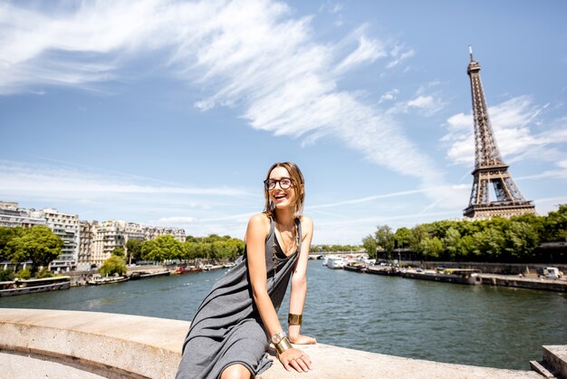 Retrato de uma jovem elegante sentada na ponte com uma bela vista da Torre Eiffel em Paris