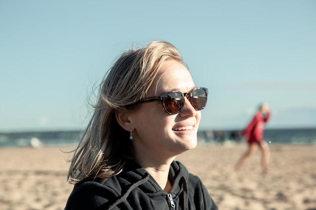 retrato de uma jovem em óculos de sol sorrindo à beira-mar ao pôr do sol