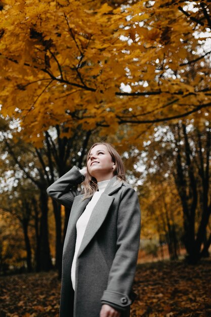 Retrato de uma jovem em um parque de outono um casaco longo cinza uma caminhada no outono