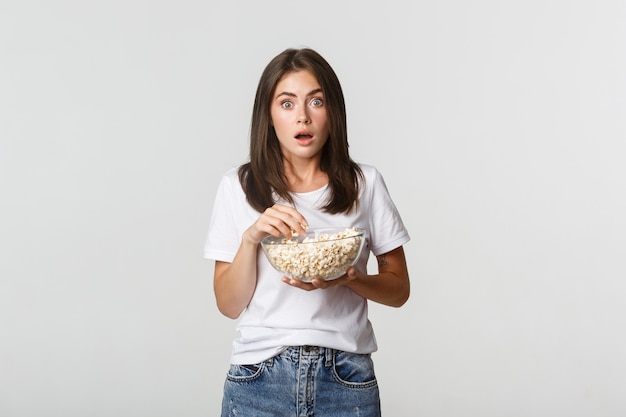 Retrato de uma jovem emocionada e espantada, comendo pipoca e assistindo filmes ou séries de TV.