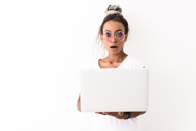 Retrato de uma jovem emocional chocada com dreads posando isolado no branco, usando o computador portátil.