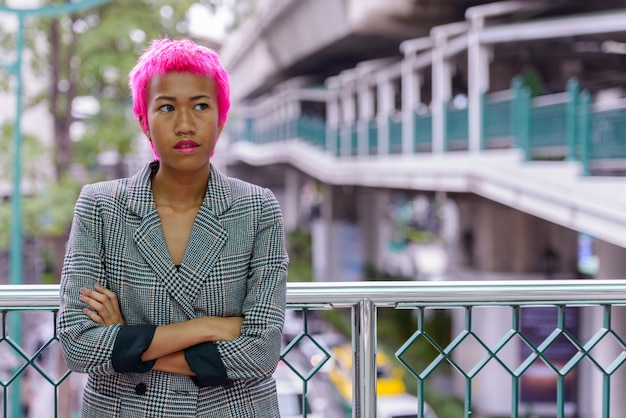 Retrato de uma jovem empresária asiática rebelde com cabelo rosa em uma ponte pedonal na cidade ao ar livre