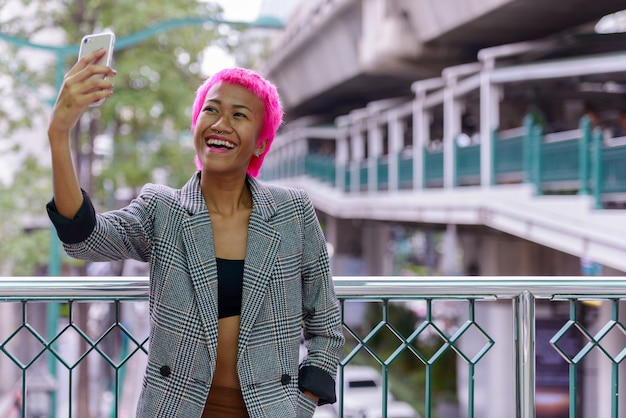 Retrato de uma jovem empresária asiática rebelde com cabelo rosa em uma ponte pedonal na cidade ao ar livre