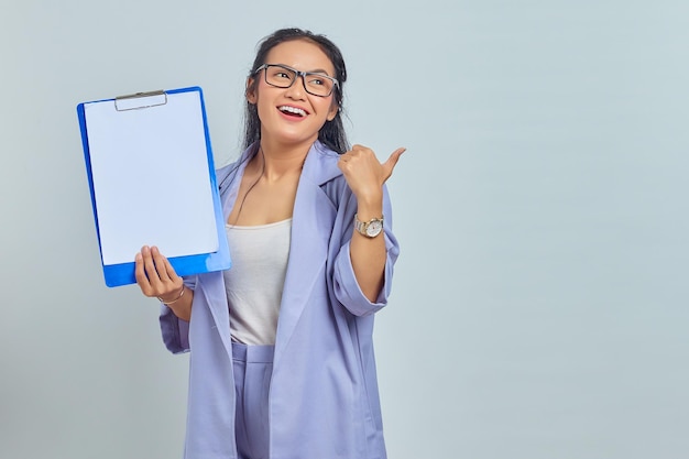 Retrato de uma jovem empresária asiática sorridente mostrando a área de transferência em branco e apontando para copiar o espaço com o dedo isolado no fundo roxo