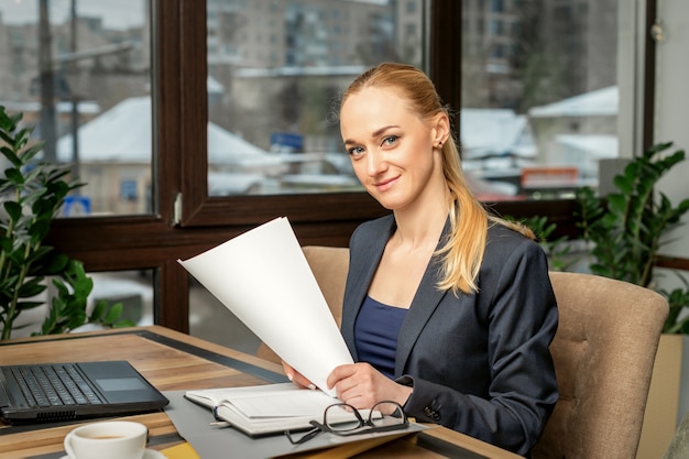 Retrato de uma jovem empresária caucasiana sorridente prepara documentos com o laptop na mesa