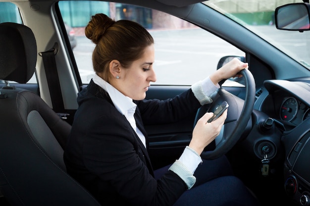 Retrato de uma jovem empresária dirigindo um carro e usando o telefone