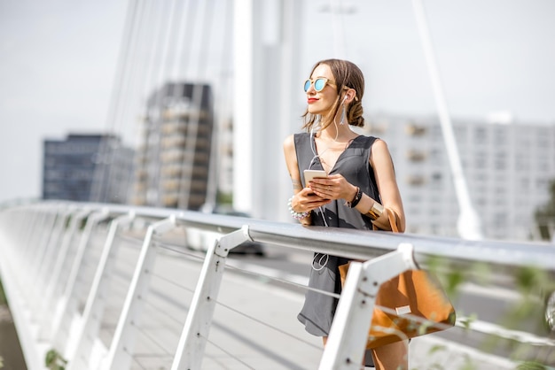 Retrato de uma jovem empresária em pé com um telefone e uma bolsa na ponte moderna na cidade de Nantes, na França