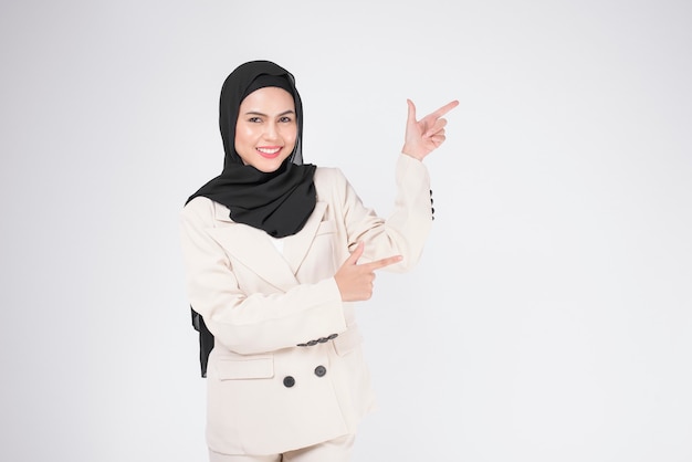 Retrato de uma jovem empresária muçulmana sorridente, vestindo terno com hijab sobre o estúdio de fundo branco.