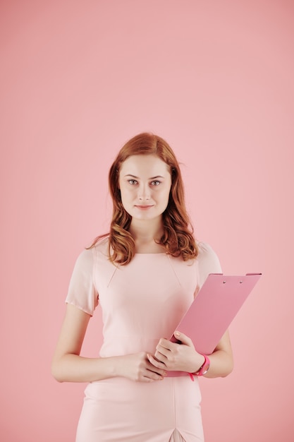 Retrato de uma jovem empresária ruiva com uma pasta posando contra um fundo rosa