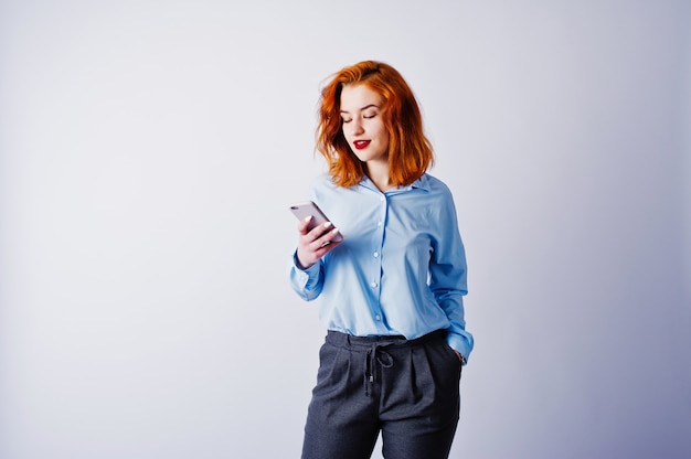 Retrato de uma jovem empresária ruiva de camisa azul e calça mandava um SMS no telefone.