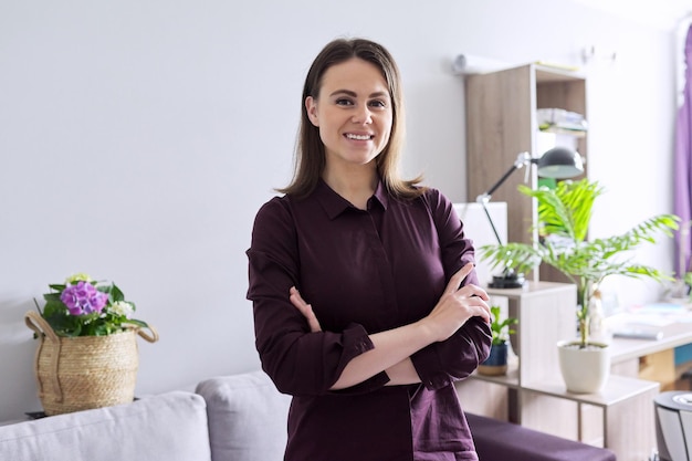 Retrato de uma jovem empresária sorridente com os braços cruzados olhando para a câmera, fundo interior da sala do armário