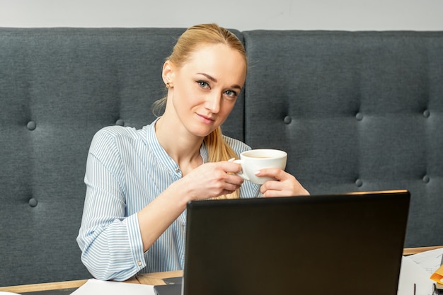 Retrato de uma jovem empresária usando laptop sentado à mesa com uma xícara de café em um café