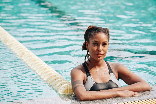 Retrato de uma jovem encantadora em pé na água à beira da piscina após o treino matinal