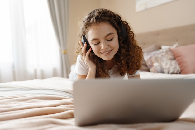 Retrato de uma jovem encaracolada usando laptop na cama em casa
