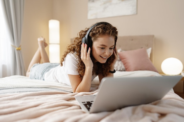 Retrato de uma jovem encaracolada usando laptop na cama em casa