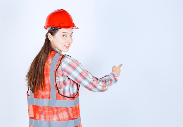 Retrato de uma jovem engenheira linda no capacete, apontando para algum lugar.