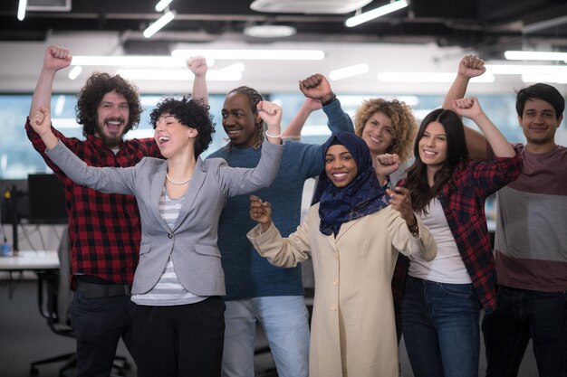 retrato de uma jovem equipe multiétnica de desenvolvedores de software, de pé, olhando para a câmera, enquanto celebra o sucesso no escritório moderno de startups