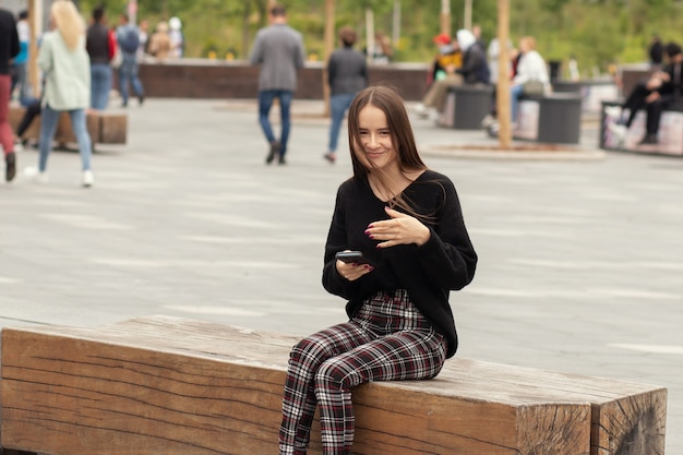Retrato de uma jovem estudante sorridente perto da universidade falando em um smartphone