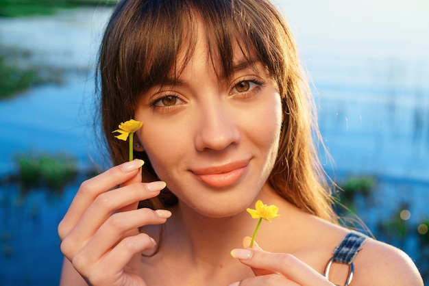 Retrato de uma jovem europeia alegre num contexto de água, segurando flores perto de seu rosto. Conceito de cosméticos naturais