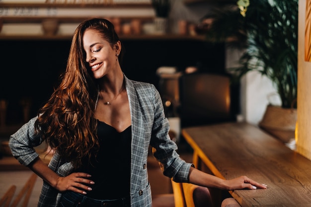 Retrato de uma jovem europeia com cabelo comprido em um café à luz da noite, uma garota alta com uma jaqueta com cabelo comprido em um café.