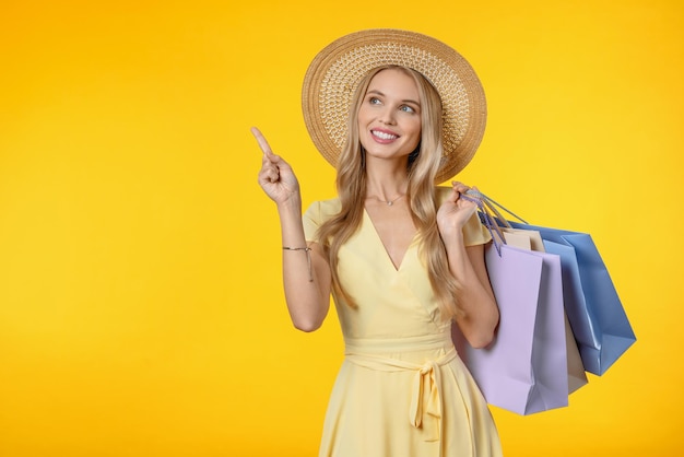 Retrato de uma jovem excitada com chapéu de verão segurando sacolas de compras e apontando
