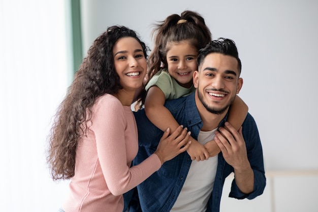 Retrato de uma jovem família árabe de três feliz com a filha pequena. Mãe, pai e filho do Oriente Médio se divertindo enquanto posam em casa, pais se divertindo com seus filhos, espaço livre