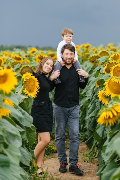 Retrato de uma jovem família linda com uma criança pequena em um campo com girassóis em um dia de verão