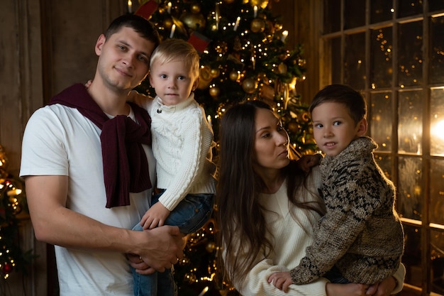 Retrato de uma jovem família sorridente com crianças pequenas perto da árvore de Natal acenando uma saudação para