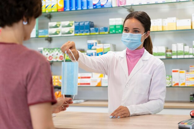 Retrato de uma jovem farmacêutica com uma máscara dando outra máscara cirúrgica a um cliente