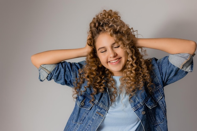 Retrato de uma jovem feliz ajustando seu cabelo loiro encaracolado com os produtos de cabelo das mãos