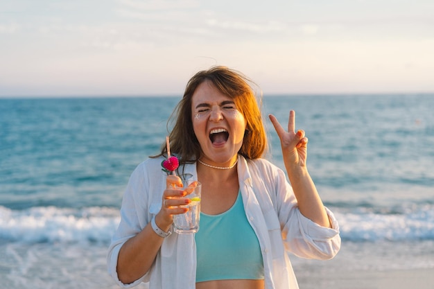 Foto retrato de uma jovem feliz com um coquetel na mão em um fundo de belo mar