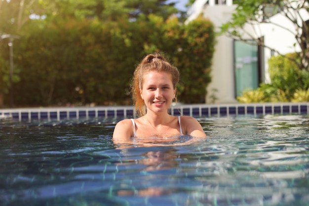 Retrato de uma jovem feliz e alegre se divertindo nadando na piscina ao ar livre no dia ensolarado de verão