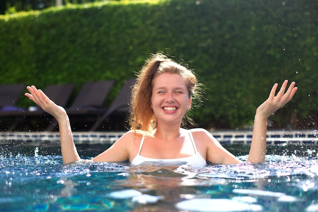 Retrato de uma jovem feliz e alegre se divertindo nadando na piscina ao ar livre no dia ensolarado de verão