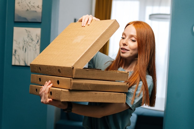 Retrato de uma jovem feliz e bonita caixa aberta de pizza quente na entrada do apartamento olhando para dentro