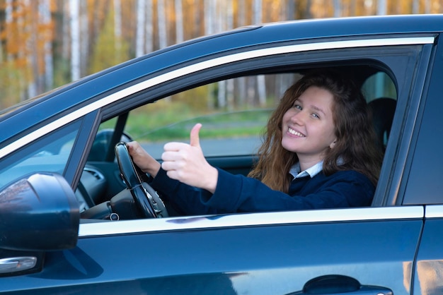 Foto retrato de uma jovem feliz e positiva motorista está sentada em seu carro novo automóvel gostando de dirigir se divertindo rindo senhora alegre no automóvel mostrando o polegar para cima como gesto