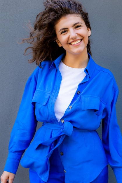 Foto retrato de uma jovem feliz em traje azul de pé contra a parede