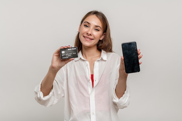 Retrato de uma jovem feliz mostrando um cartão de crédito de plástico segurando um telefone celular com tela preta