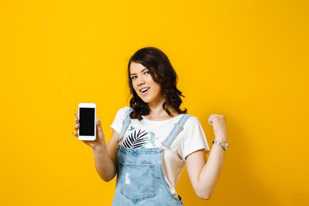 Retrato de uma jovem feliz, olhando para o telefone móvel e isolado sobre parede amarela