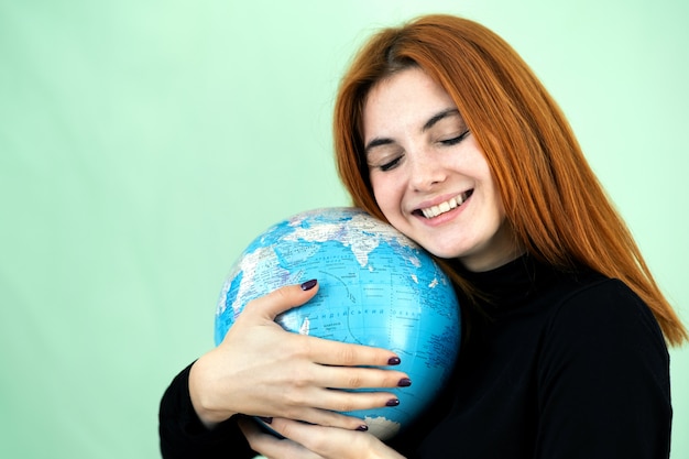 Retrato de uma jovem feliz, segurando o globo geográfico do mundo nas mãos dela. Destino de viagem e conceito de proteção do planeta.