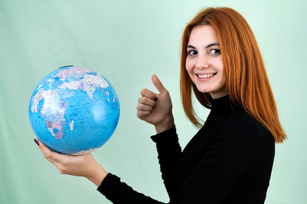 Foto retrato de uma jovem feliz segurando o globo geográfico do mundo nas mãos.