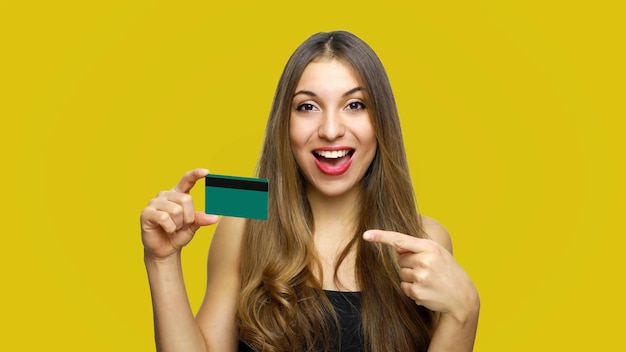 Foto retrato de uma jovem feliz segurando um cartão de crédito contra um fundo amarelo