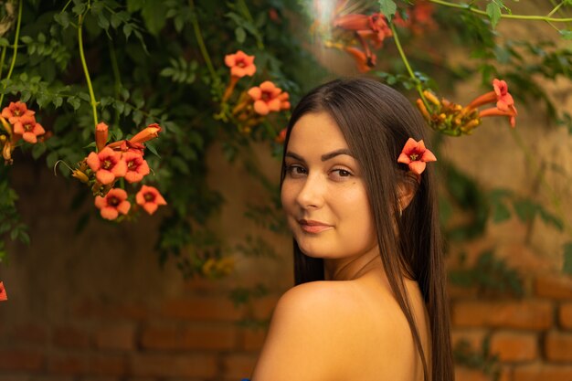 Retrato de uma jovem feliz vestindo um vestido azul e parada nas flores do campis radicans.