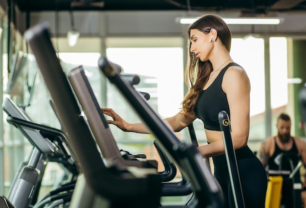 Retrato de uma jovem fitness em roupas esportivas exercitando-se em uma máquina cardio moderna com toque sc